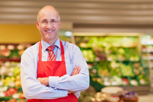 The owner of a supermarket smiling in front of a produce display.