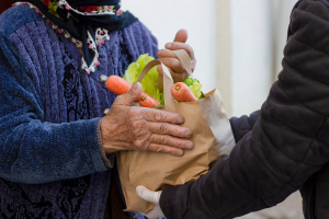 An older person receiving a paper bag of fresh food.