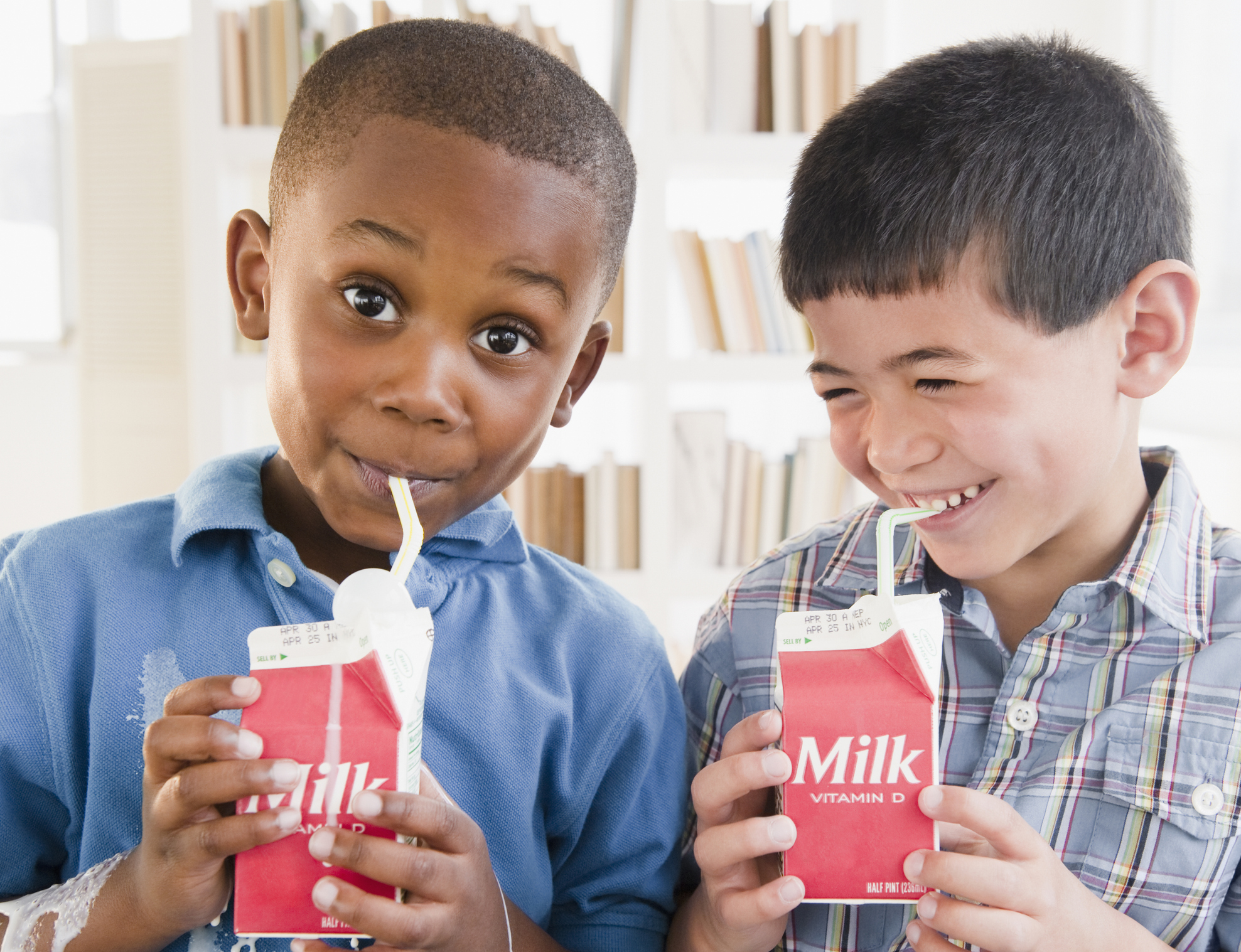 Dos niños bebiendo cartones de leche.